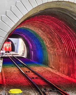 A tunnel that is lit up like a rainbow, with a red cable car approaching it.