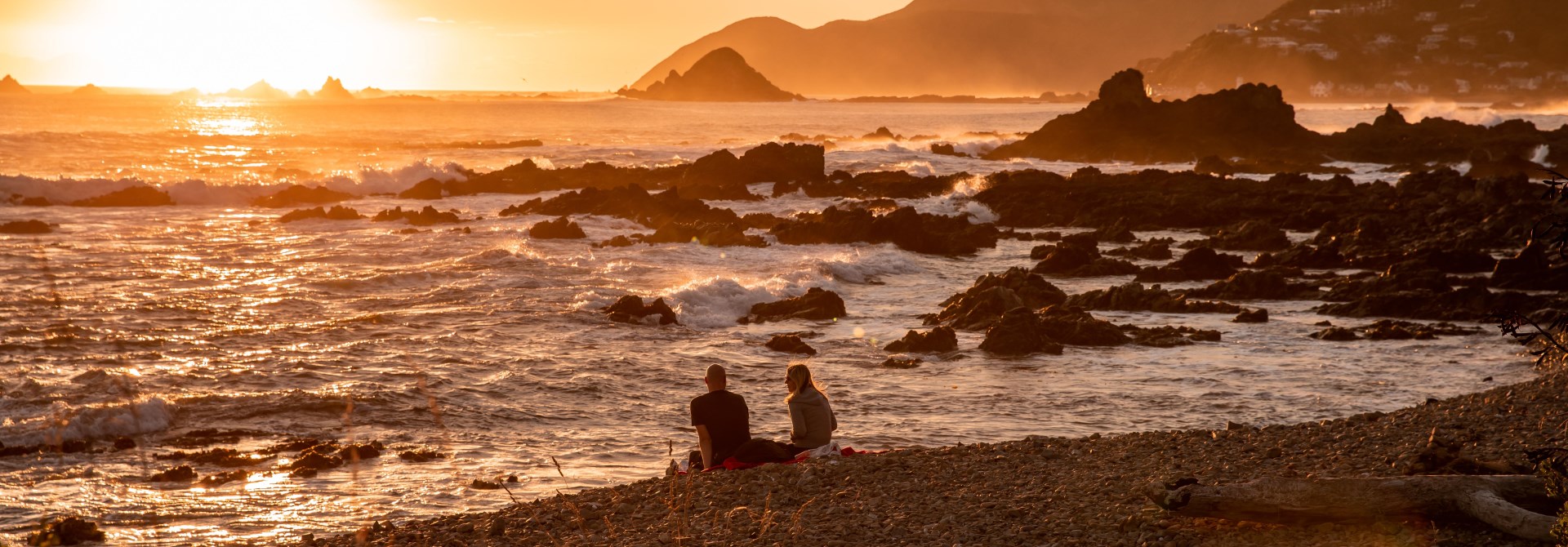 Two people sitting on the beach at sunset.