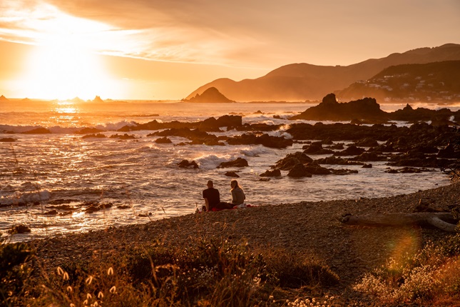 Two people sitting on the beach at sunset.