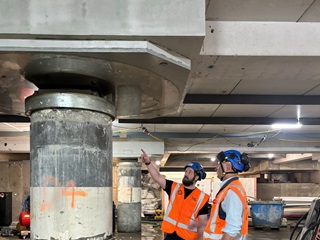 Two men standing infront of a concrete pillar.