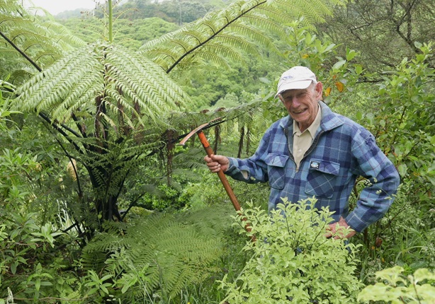 A man holding out gardening equipment in a bush.