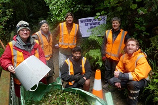 Group of people in high vis clothing all holding gardening equipment and smiling.