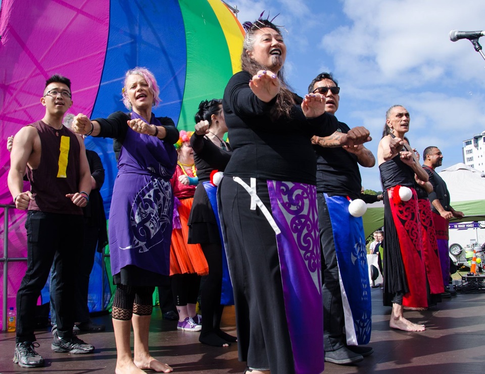 Group dancing and singing in front of a rainbow flag.