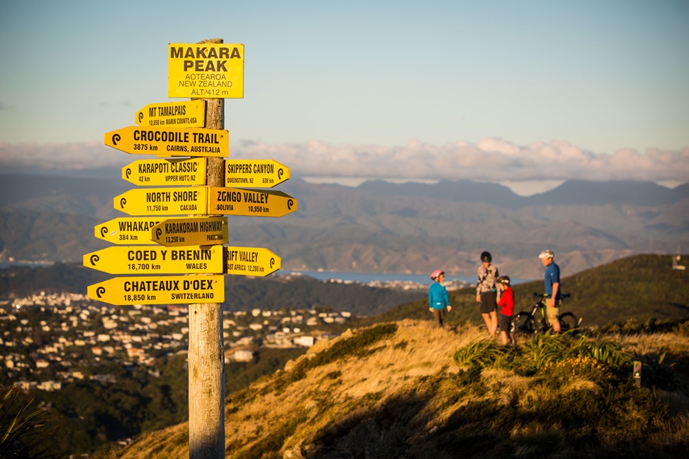 Signs on top of Makara Peak with people on bikes behind it.