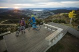 Two people leaning on bikes on a wooden platform on the top of a hill.