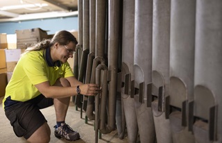 Woman in a high vis tshirt examining one of the 16’ reed resonators from the Town Hall organ.