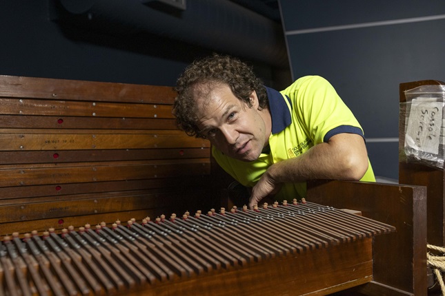 Man leaning over the top of an organ in a yellow high vis top.