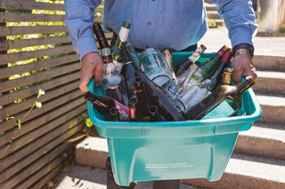 Image of person carrying their glass recycling bin.