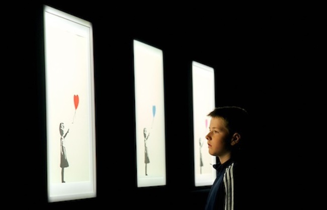 Young man looking at Girl With Balloon Banksy artwork at exhibition