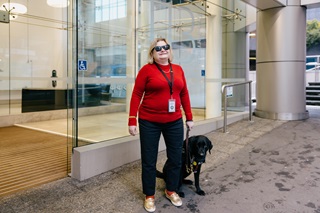 Image of Bonnie Mosen and her black labrador guide dog, Eclipse. Bonnie and eclipse are outside of the Council offices
