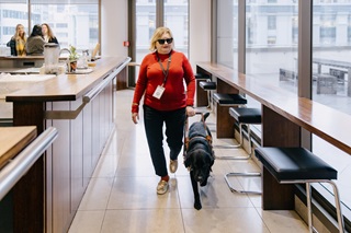 Image of Bonnie Mosen and her black labrador guide dog, Eclipse. Bonnie and eclipse are walking through a quiet cafe