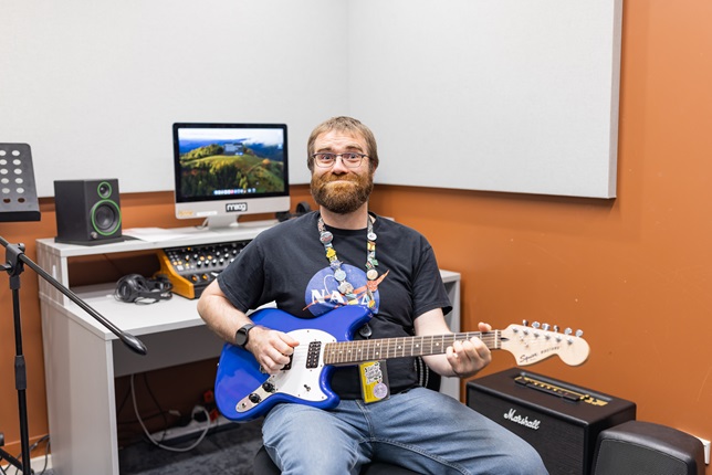 Image of Jamie sitting in a recording space with a blue electric guitar