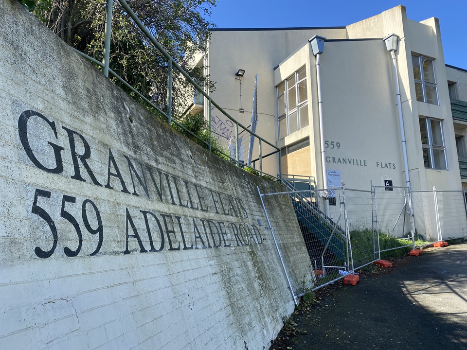 Entrance and driveway to Granville apartments with fencing around building in background.