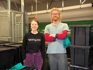 A man and a woman standing infront of a composting machine.