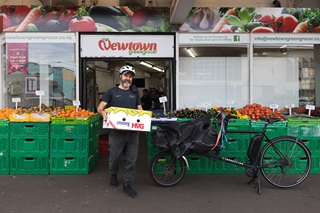 Man in motion outside of a grocers store, carrying a fruit box on the way to an electric bike.