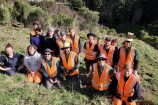 A group of people kneeling down on the side of a hill with vegetation around them.