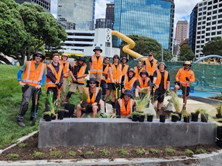 A group of gardeners smiling behind a concrete block with plants resting on top and around them.