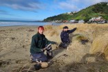 Two gardeners working on sand dunes on the edge of a beach.