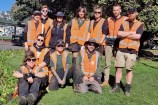 A group of nine people wearing high vis vests and gardening uniforms, standing on grass.