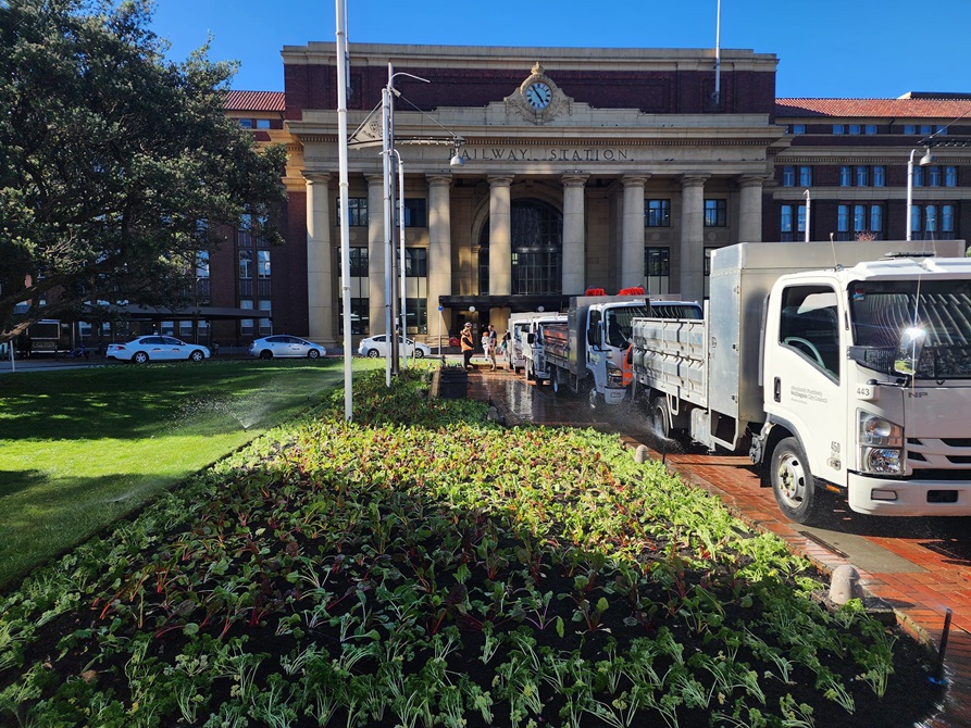 A view of plants infront of the railway station with a gardening truck to one side.