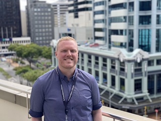 A man wearing a blue shirt, standing infront of Lambton Quay.