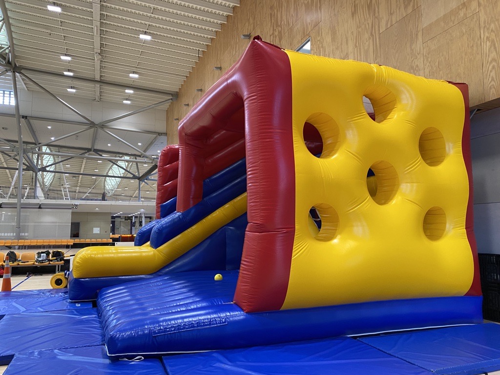 Large blue inflatable with a yellow wall set up at a sports centre.
