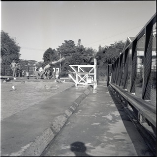 Black and white archive photo of a person diving into an outdoor pool.