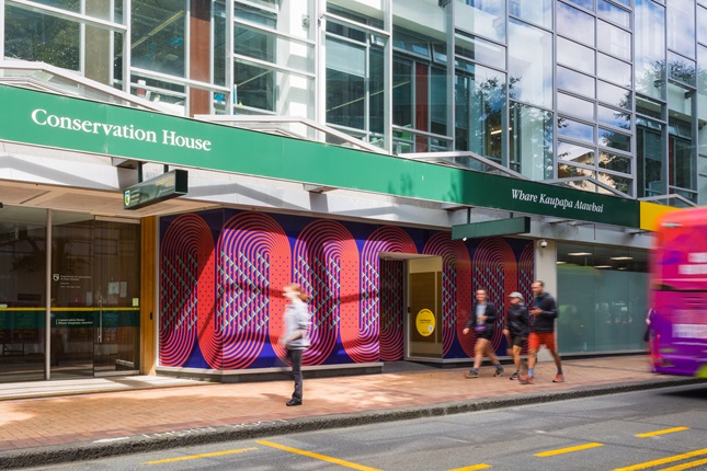 People walking down the street with artwork in the windows of the shops next to them.