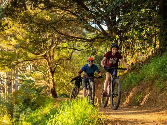 Two people riding their bikes on a track in the bush.