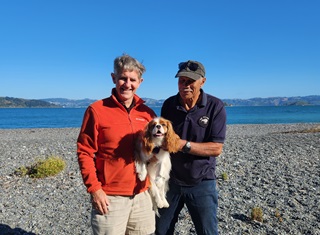 Two people standing on a beach holding onto a small orange and white dog.