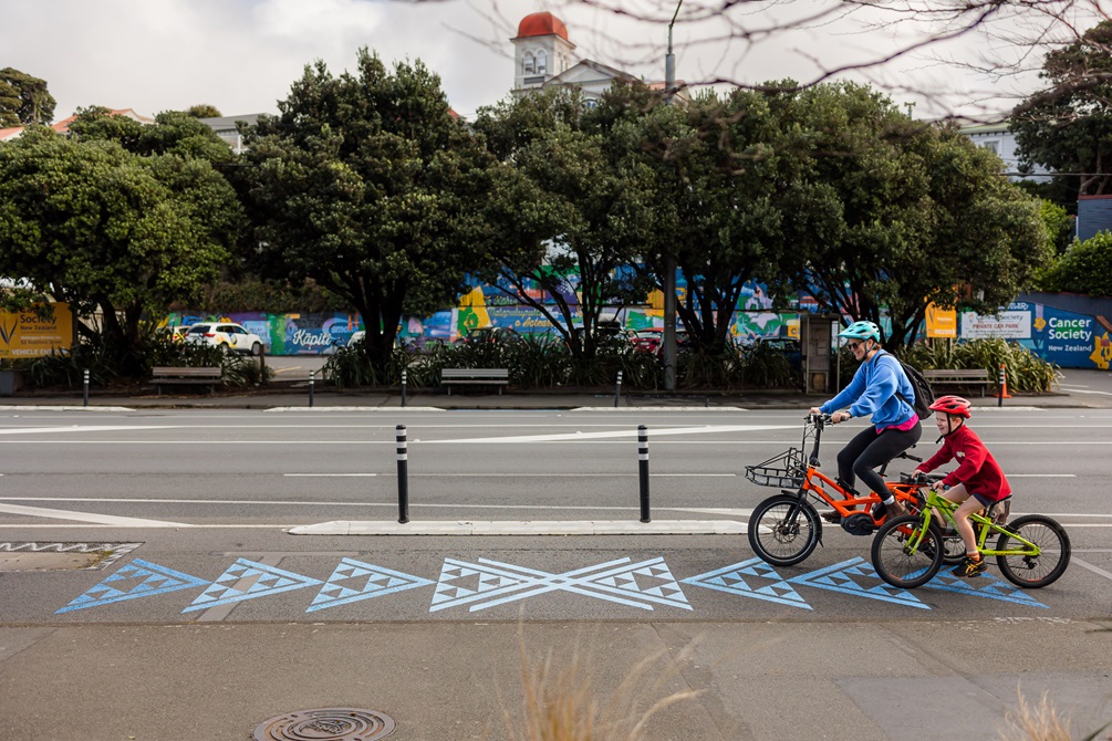 An adult and a child cycling in a bike lane with awa markings on the ground.