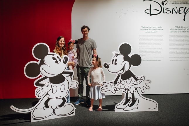 Family pose with Mickey and Minnie Mouse at entrance to Disney exhibition.