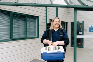 A woman in a blue shirt with a black vest holding a pet carrier.