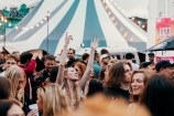 In the background there is a blue and white tent top, and infront there is a crowd of people dancing and socialising. 