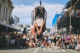 Acrobat dangling upside down infront of a crowd of people.