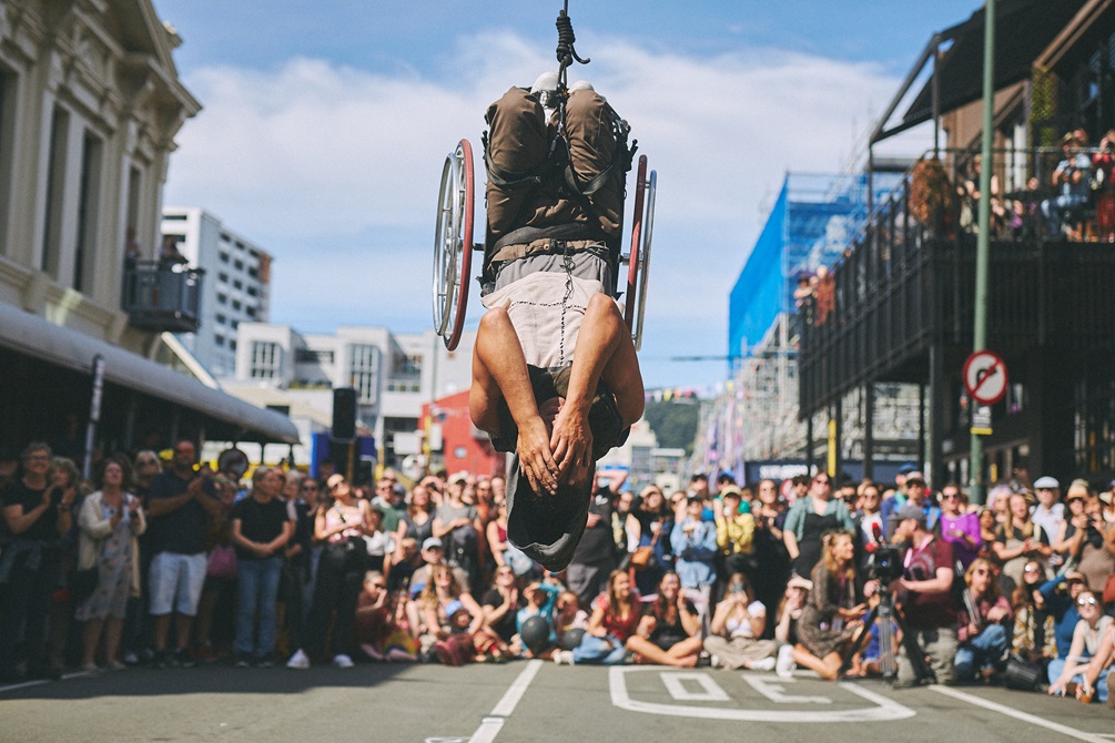 Acrobat dangling upside down infront of a crowd of people.