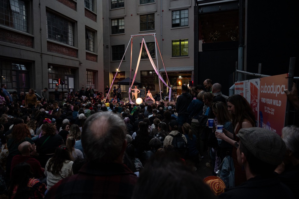 A crowd of people watching performers on a small stage in the distance.