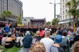 A group of people sitting down watching a kapa haka group perform on a stage.