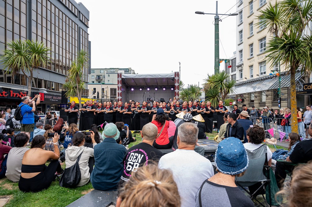 A group of people sitting down watching a kapa haka group perform on a stage.