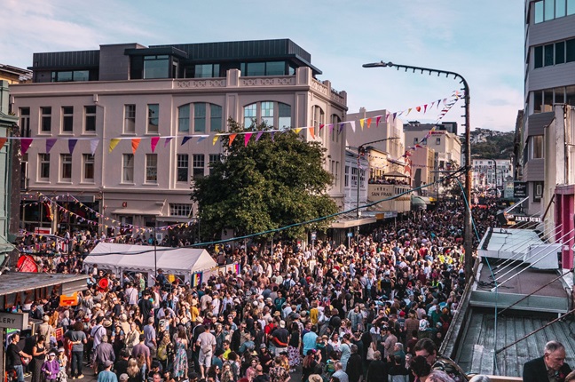 Crowds of people gathered in the streets with flag bunting strung over the top of them.