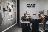 Three people looking into a Zoetrope at the Disney Exhibition with Steamboat Willie on the wall.