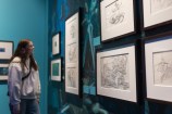 A person in a hoodie looking at sketches on a wall.