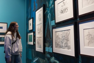 A person in a hoodie looking at sketches on a wall.