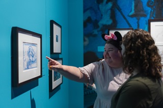 Two people looking at sketches on a wall, and pointing at them.