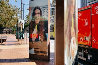 A reflective glass panel shows a person's image, with a city street and red vehicle in the background.