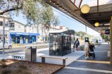 Bus shelter in the middle of an urban street with pedestrians walking around it.