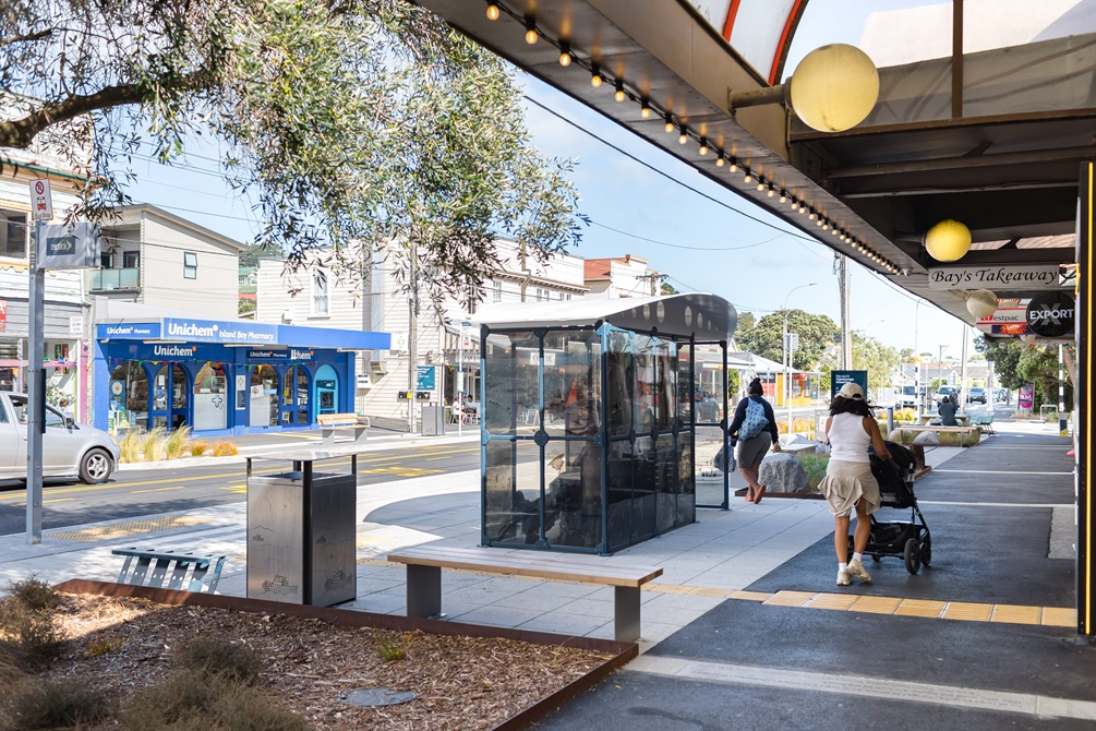 Bus shelter in the middle of an urban street with pedestrians walking around it.