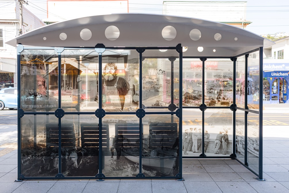 Bus shelter in the middle of an urban street with archival images on it.