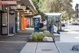 Urban streetscape with rocks in a garden and a bus shelter in the background.