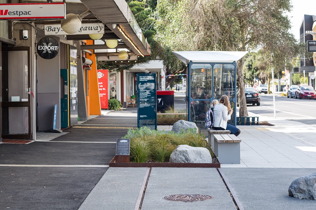 Urban streetscape with rocks in a garden and a bus shelter in the background.
